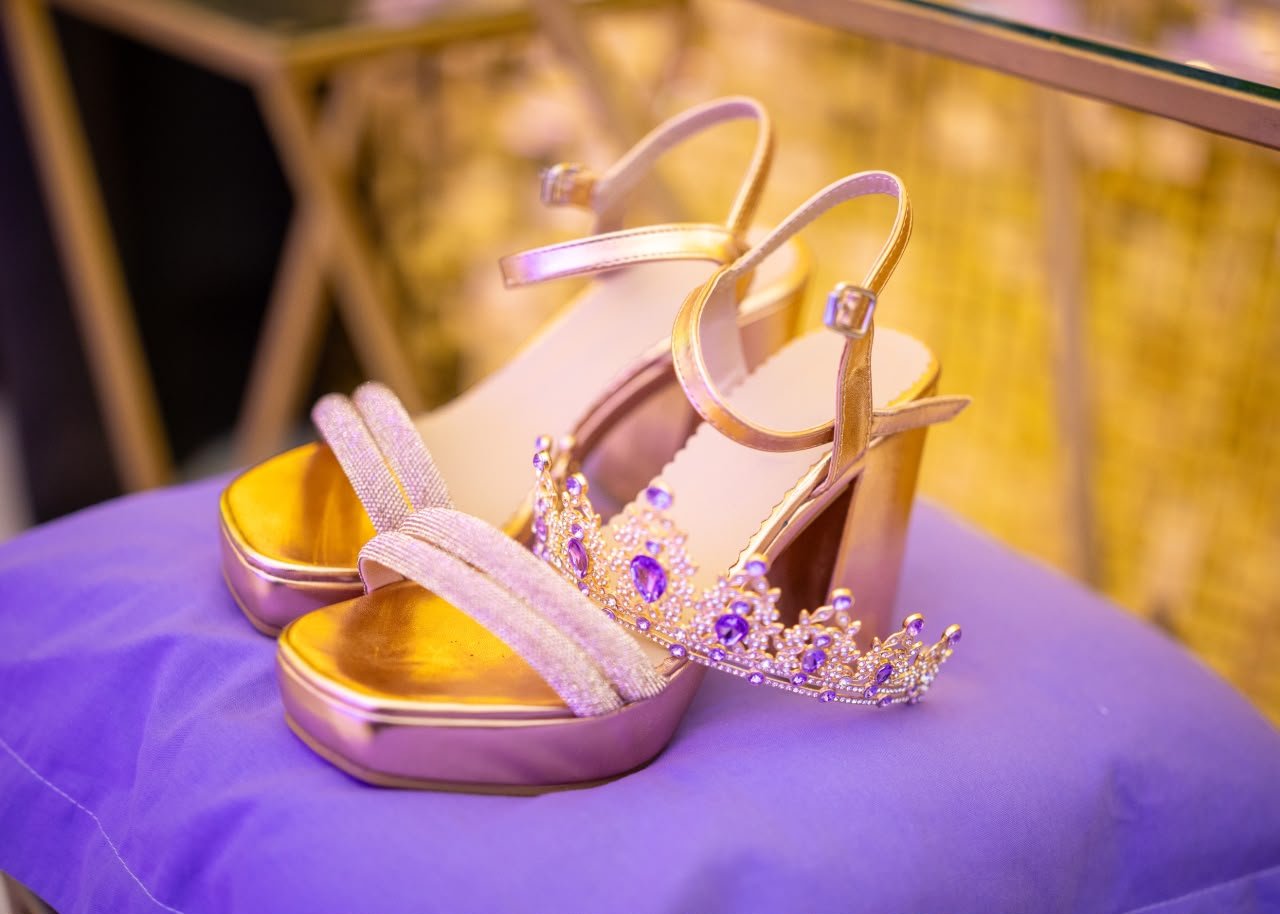 Sandalias doradas y corona de quinceañera con piedras violetas sobre un almohadón